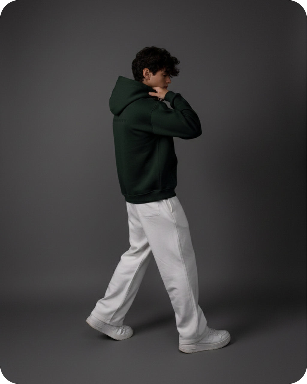 Person wearing a dark green hoodie and light gray pants on a gray background