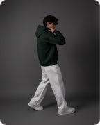 Person wearing a dark green hoodie and light gray pants on a gray background
