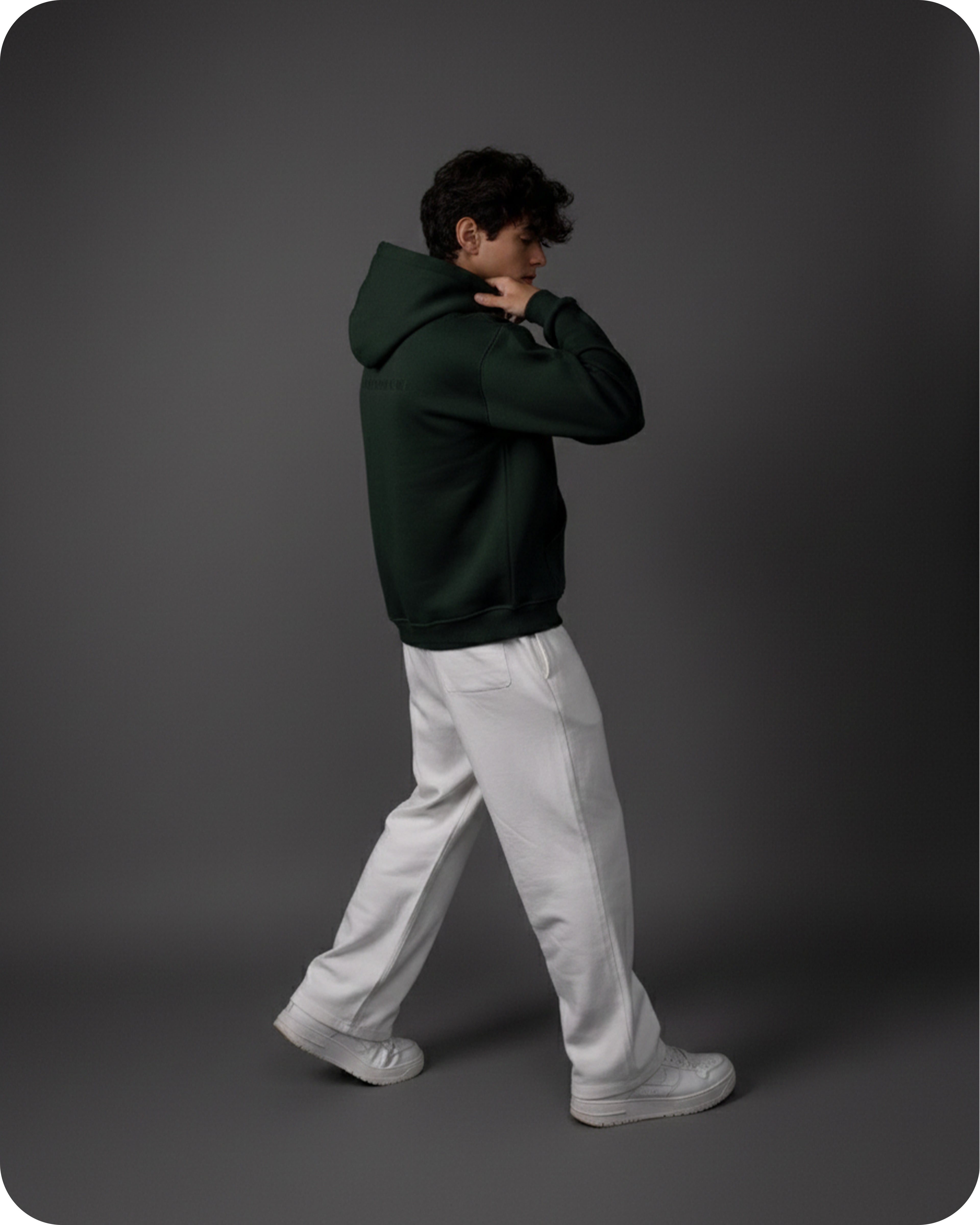 Person wearing a dark green hoodie and light gray pants on a gray background