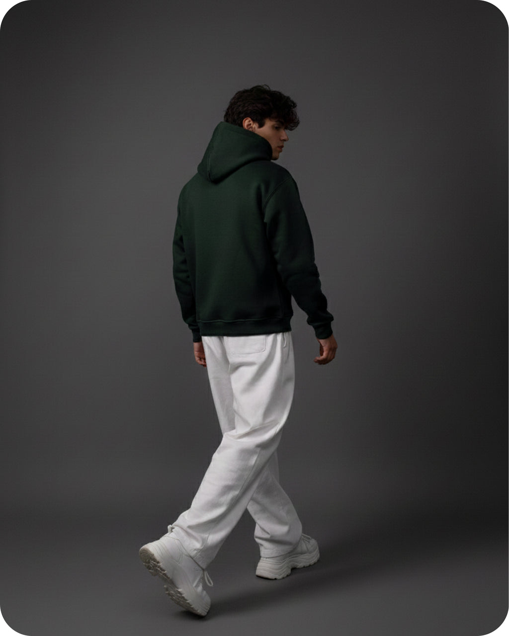 Person wearing a dark green hoodie and white pants walking on a gray background