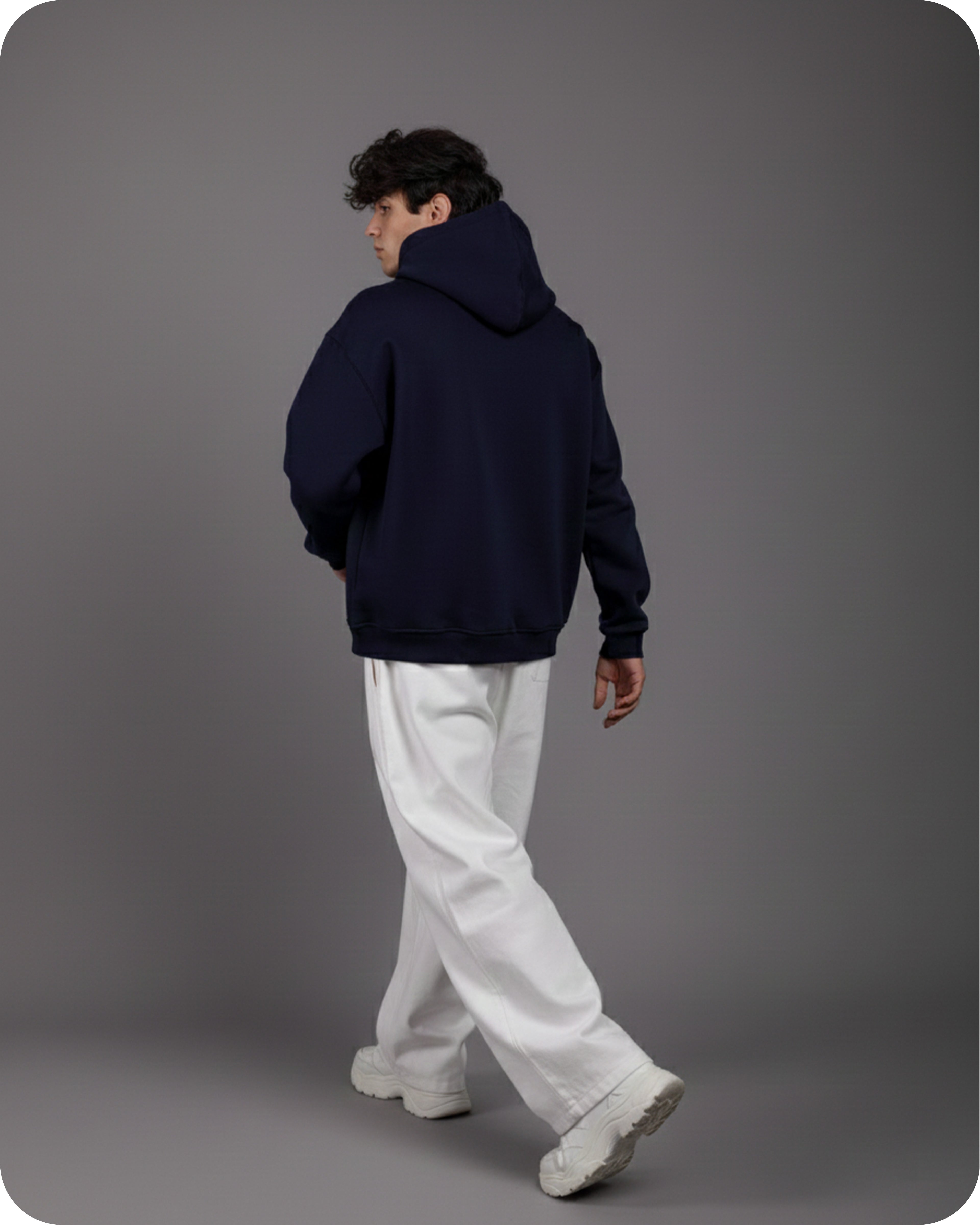 Person wearing a navy hoodie and white pants on a gray background