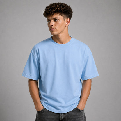 A man wearing a light blue crew-neck t-shirt and dark gray jeans, standing against a solid gray studio background.