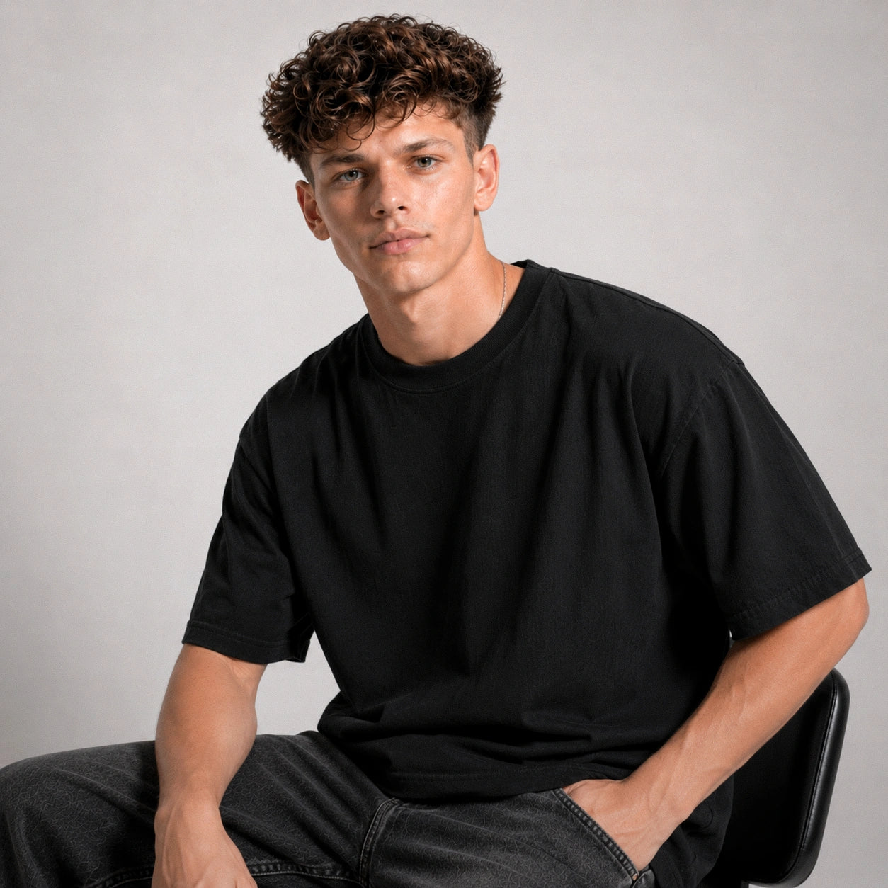 Man wearing a black t-shirt sitting against a plain background