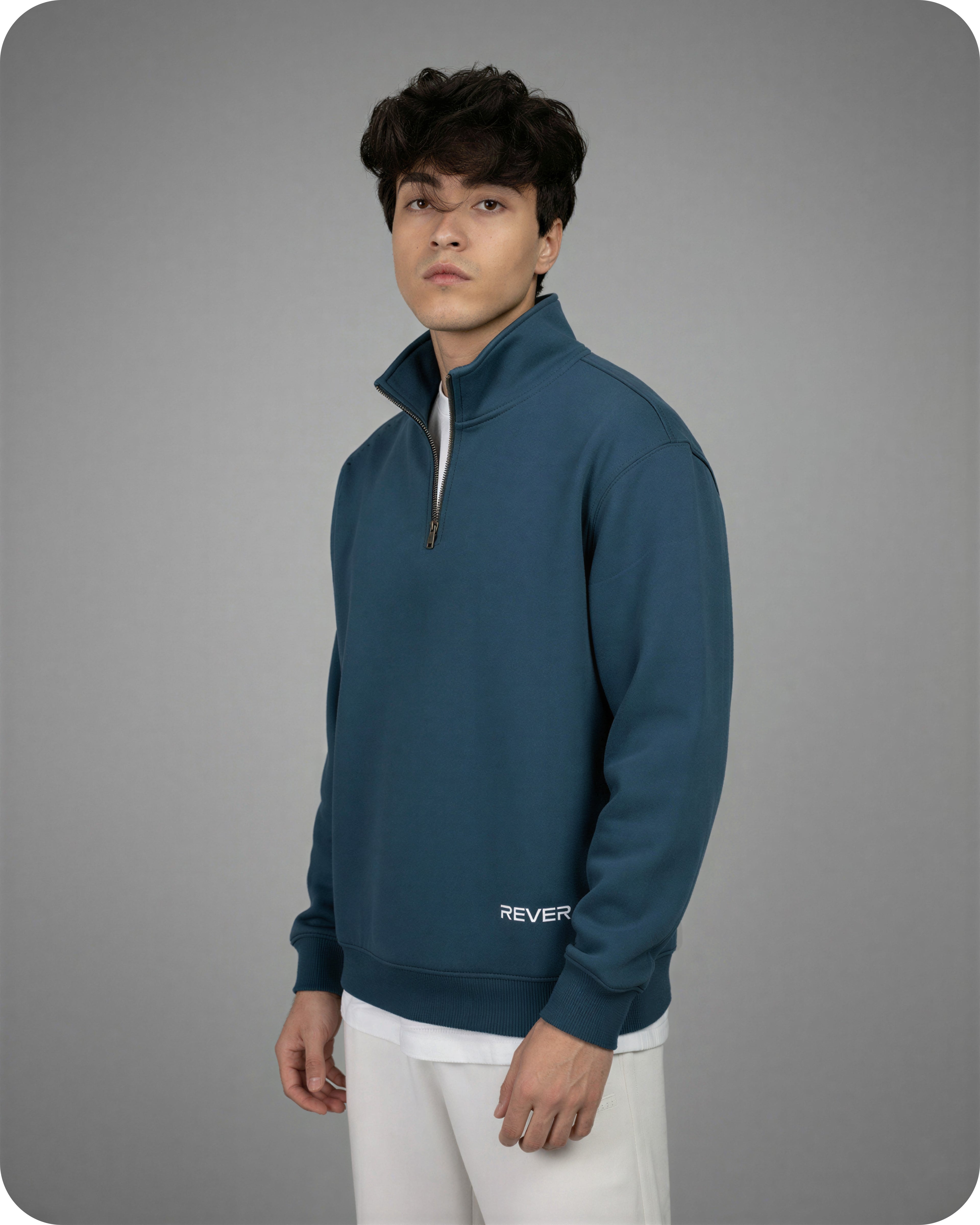Person wearing a teal pullover with 'REVER' branding on a gray background