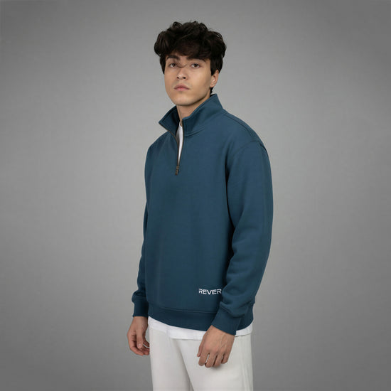 Person wearing a teal pullover with 'REVER' branding on a gray background