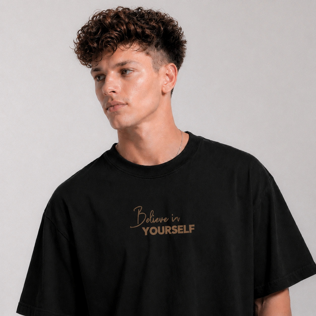 Person wearing a black t-shirt with 'Believe in Yourself' text on a plain background