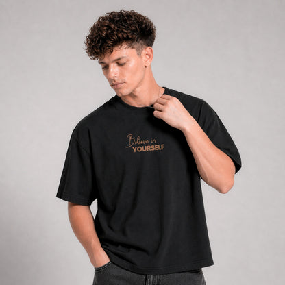 Person wearing a black t-shirt with 'Believe in Yourself' text on a gray background