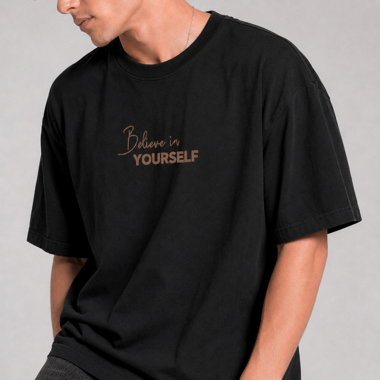 Person wearing a black t-shirt with 'Believe in Yourself' text on a plain background
