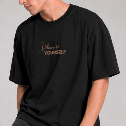 Person wearing a black t-shirt with 'Believe in Yourself' text on a plain background