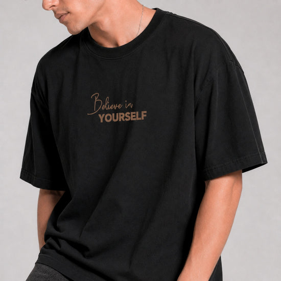 Person wearing a black t-shirt with 'Believe in Yourself' text on a plain background