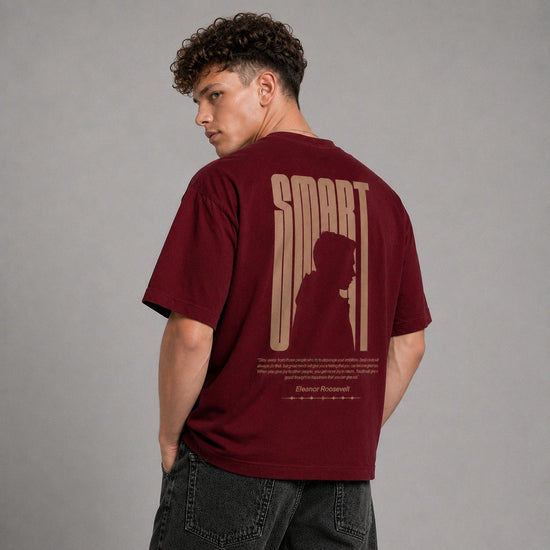 A man wearing a maroon t-shirt with a large beige graphic print on the back, photographed from behind against a neutral gray background.