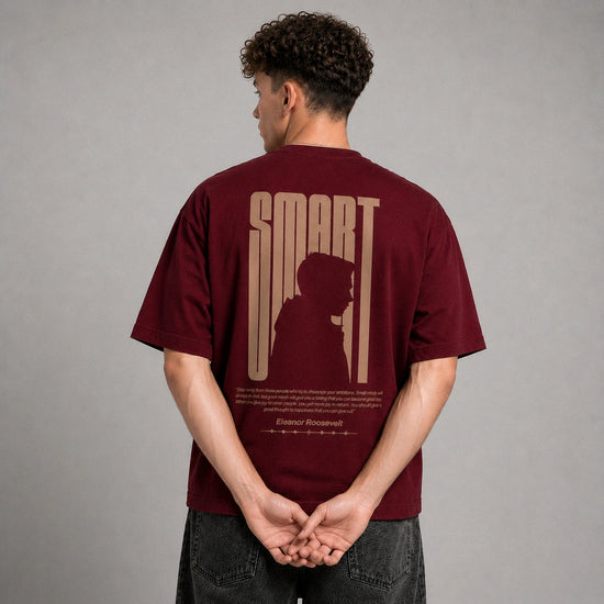 A man viewed from behind wearing a maroon t-shirt with a beige graphic print on the back that reads 'SMART' and features a silhouette of a person. The background is a solid gray studio backdrop.