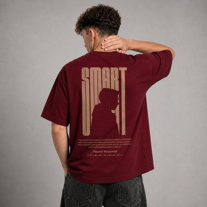 A man wearing a maroon t-shirt with a large beige graphic print on the back, shown from behind against a neutral gray background.