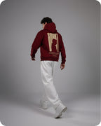 Person wearing a maroon hoodie with a logo on the back against a gray background