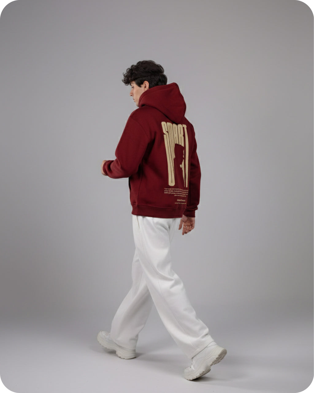 Person wearing a maroon hoodie with a design on the back, standing against a gray background