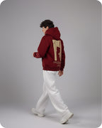Person wearing a maroon hoodie with a design on the back, standing against a gray background