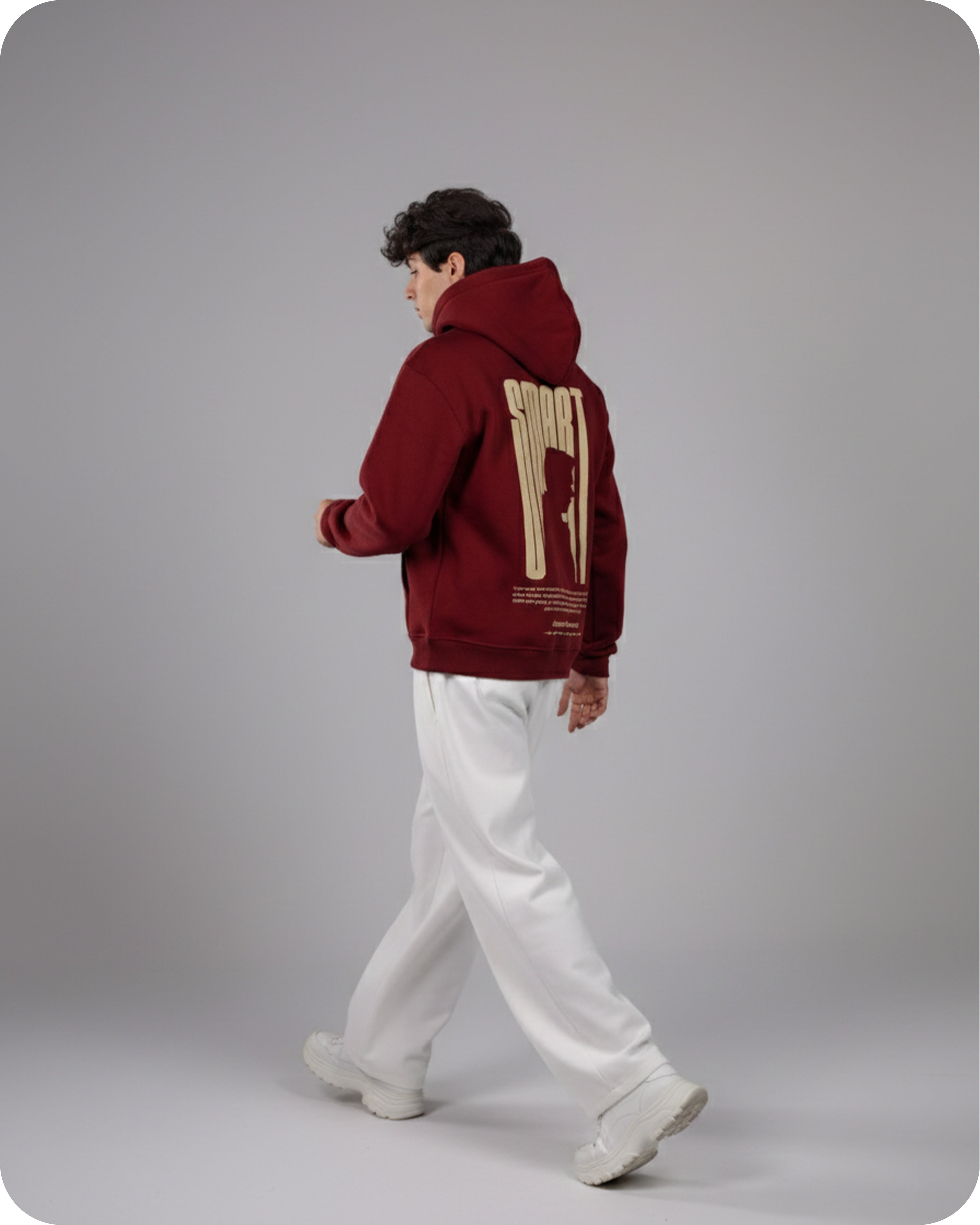 Person wearing a maroon hoodie with a design on the back, standing against a gray background