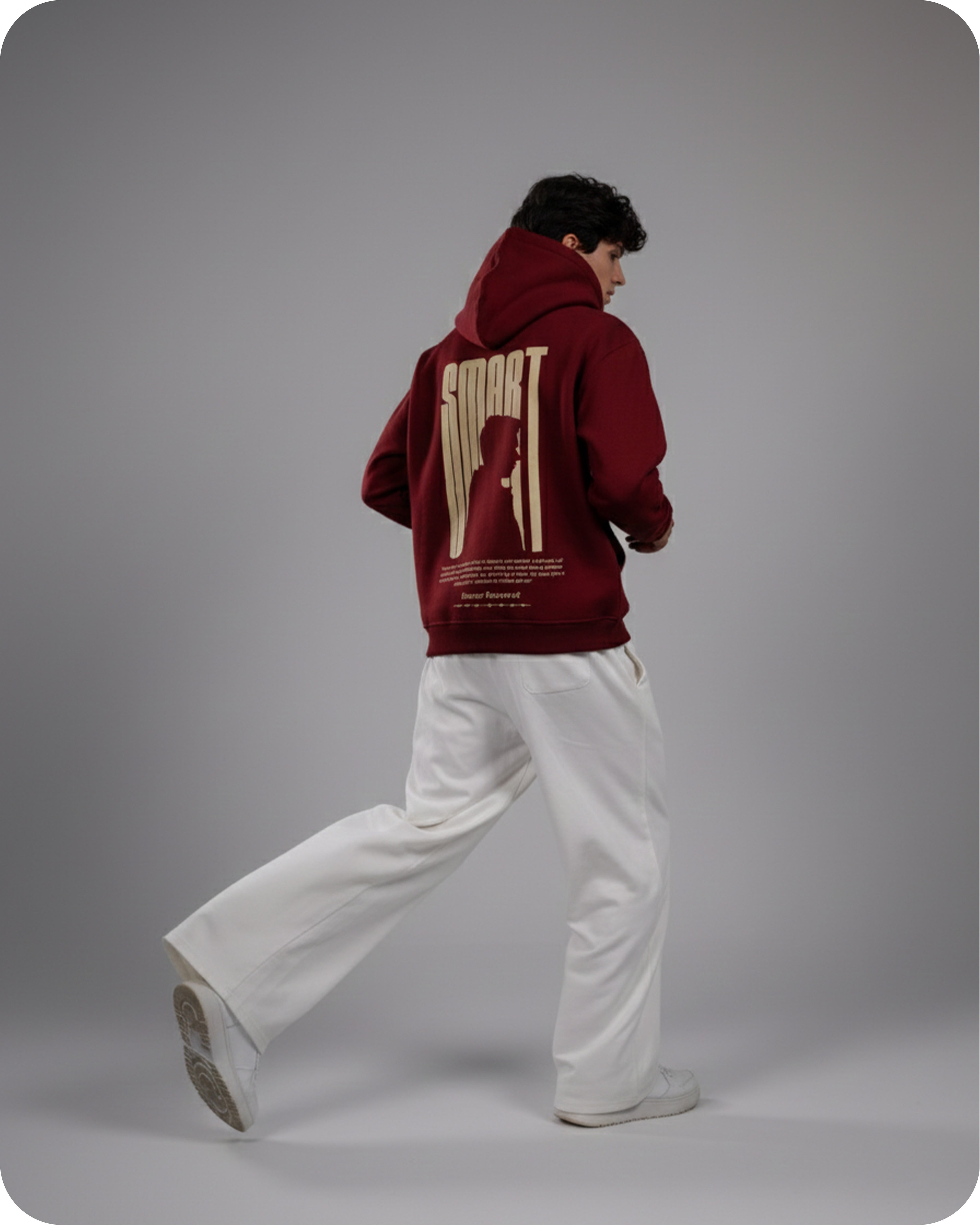 Person wearing a maroon hoodie with a logo on the back, standing against a gray background