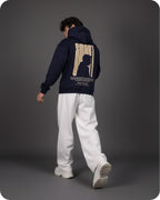 Person wearing a navy hoodie with a silhouette design on the back, standing against a gray background