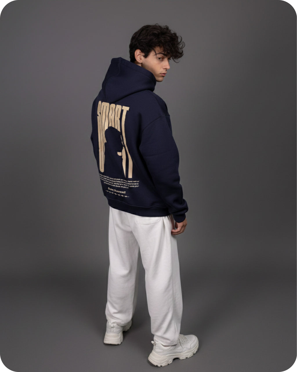 Person wearing a navy hoodie with a graphic design on the back, standing against a gray background