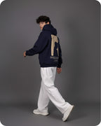 Person wearing a dark blue hoodie with a beige design on the back against a gray background