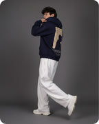 Person wearing a navy blue hoodie with a graphic design on the back, white pants, and white shoes against a gray background.