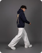 Person wearing a navy hoodie with a graphic design on the back, white pants, and white shoes against a gray background