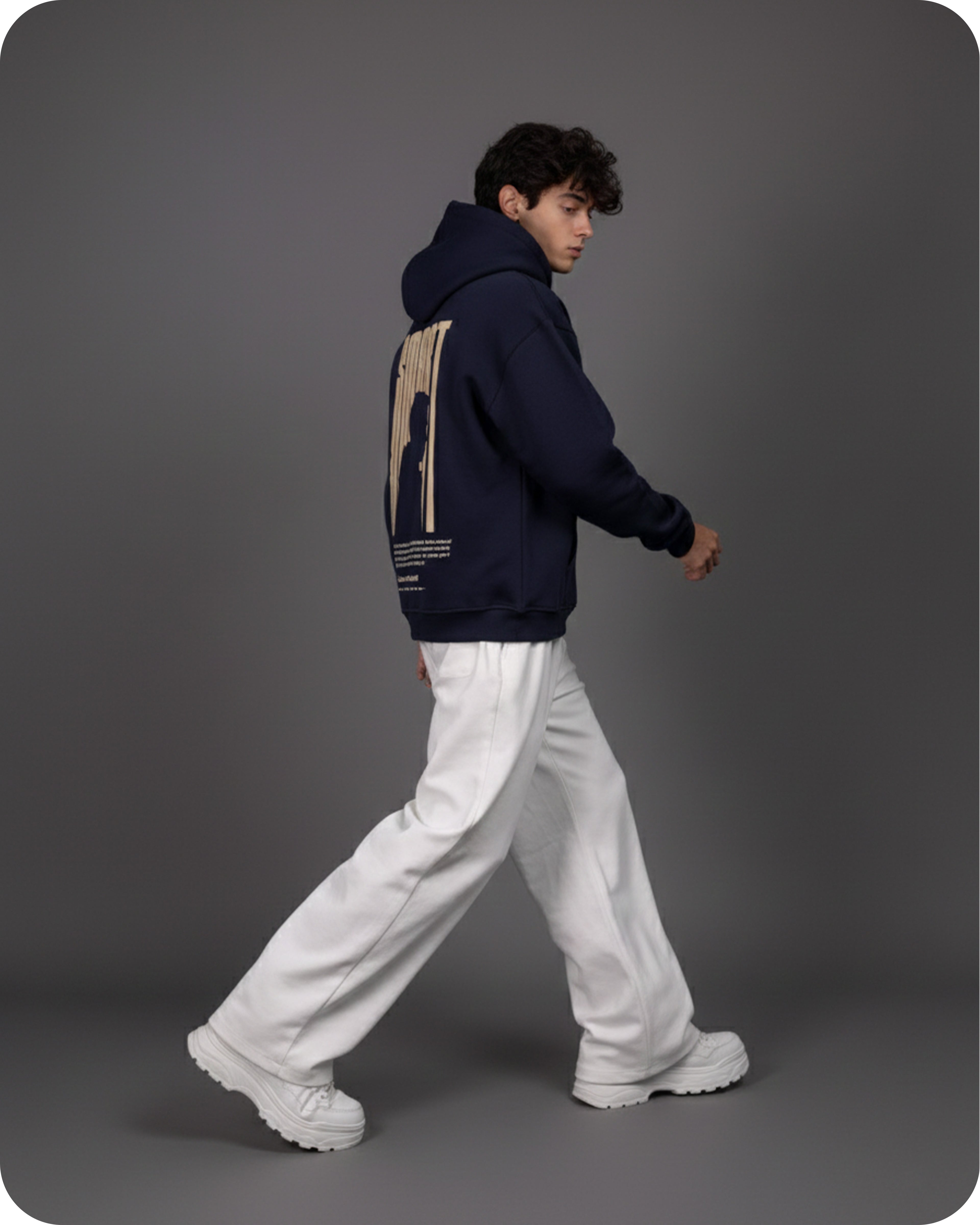 Person wearing a navy hoodie with a graphic design on the back, white pants, and white shoes against a gray background