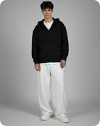 Person wearing a black hoodie and white pants on a gray background
