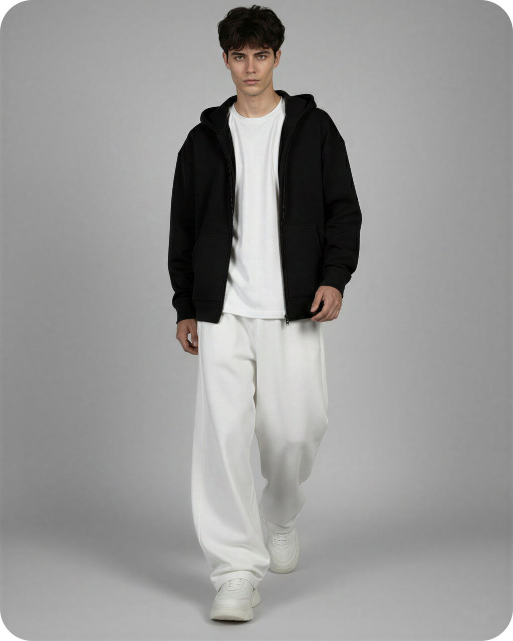 Person wearing a black hoodie, white t-shirt, and white pants on a gray background