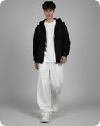 Person wearing a black hoodie, white t-shirt, and white pants on a gray background