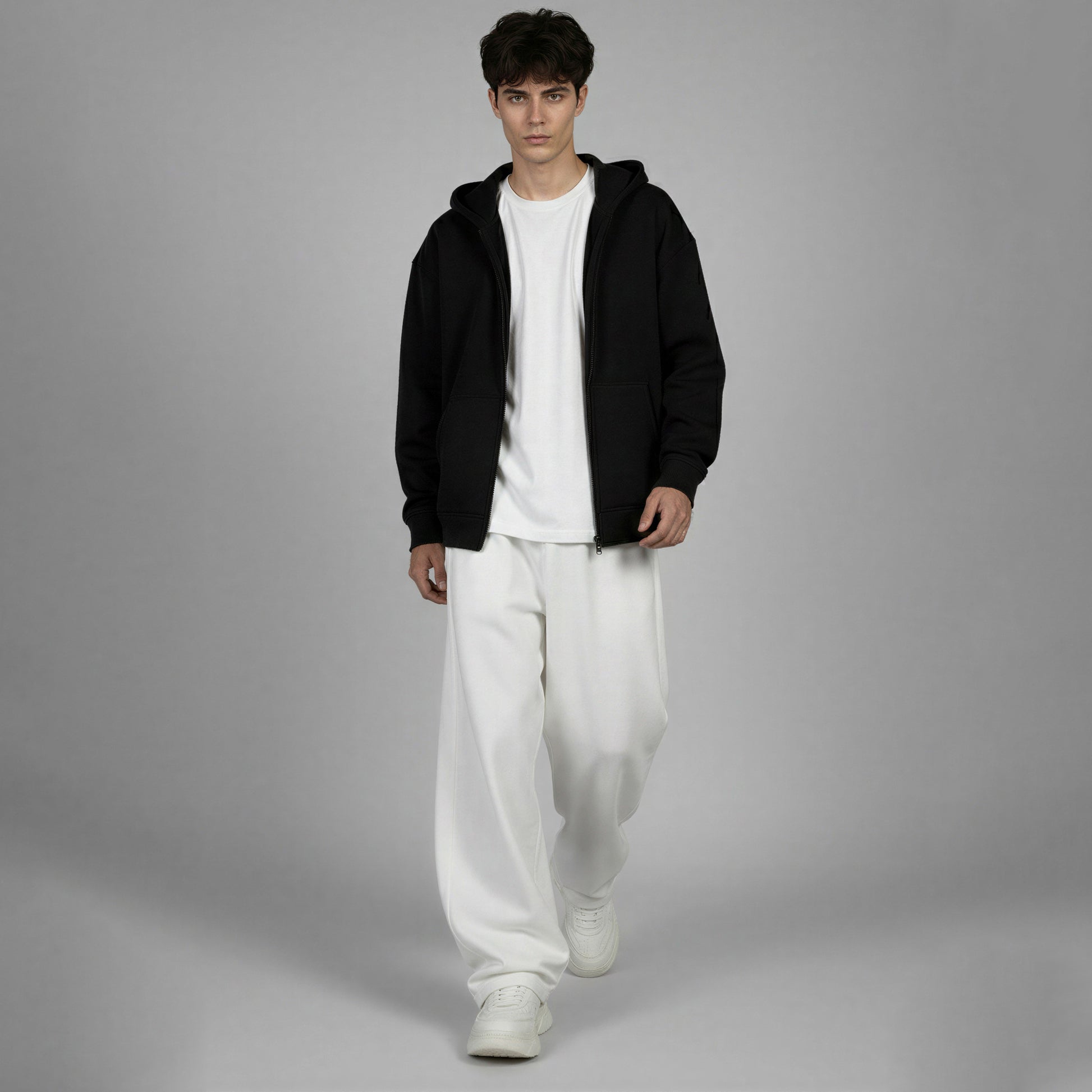Person wearing a black hoodie, white t-shirt, and white pants on a gray background