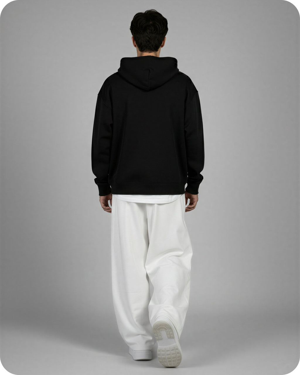 Person wearing a black hoodie and white pants on a gray background