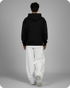 Person wearing a black hoodie and white pants on a gray background
