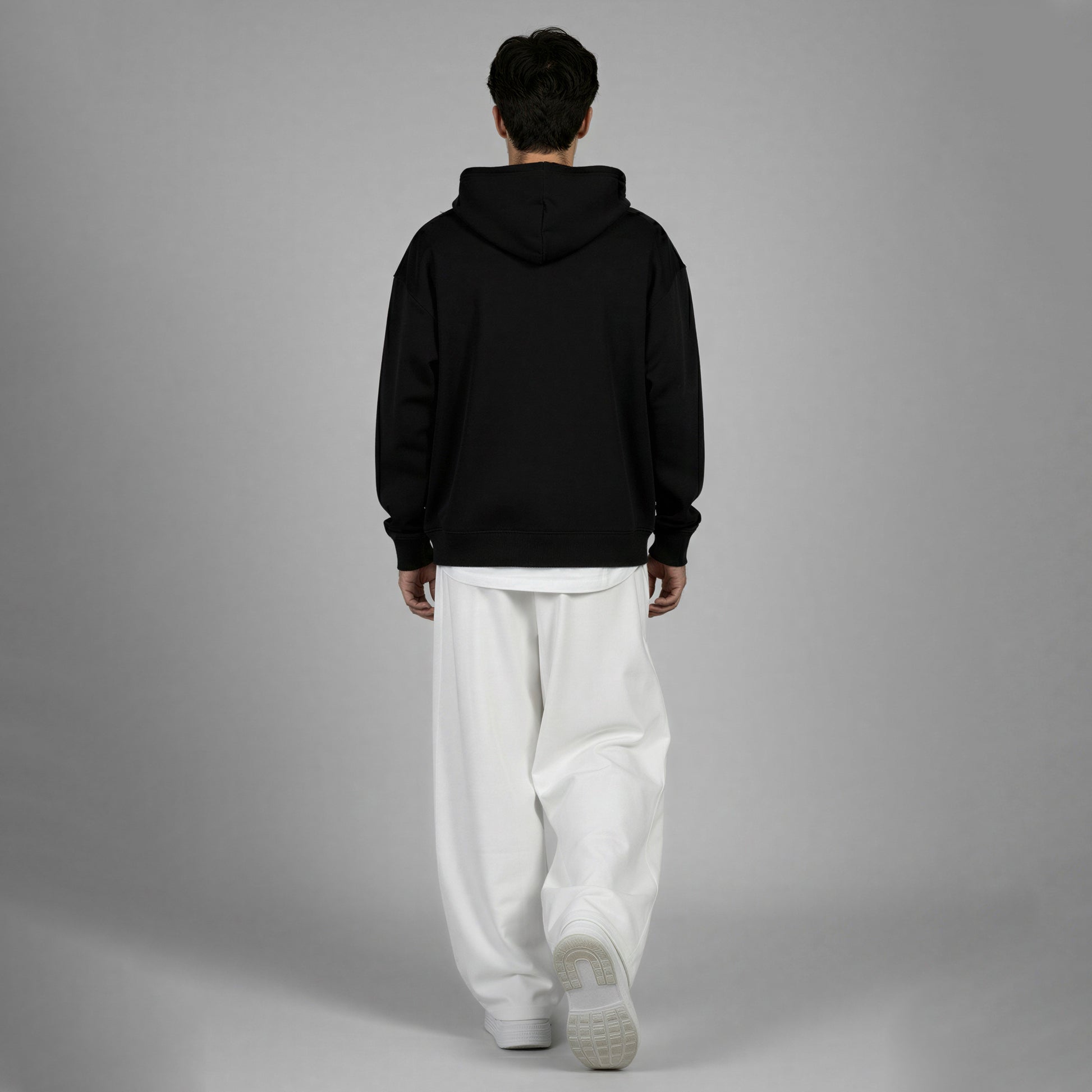 Person wearing a black hoodie and white pants on a gray background