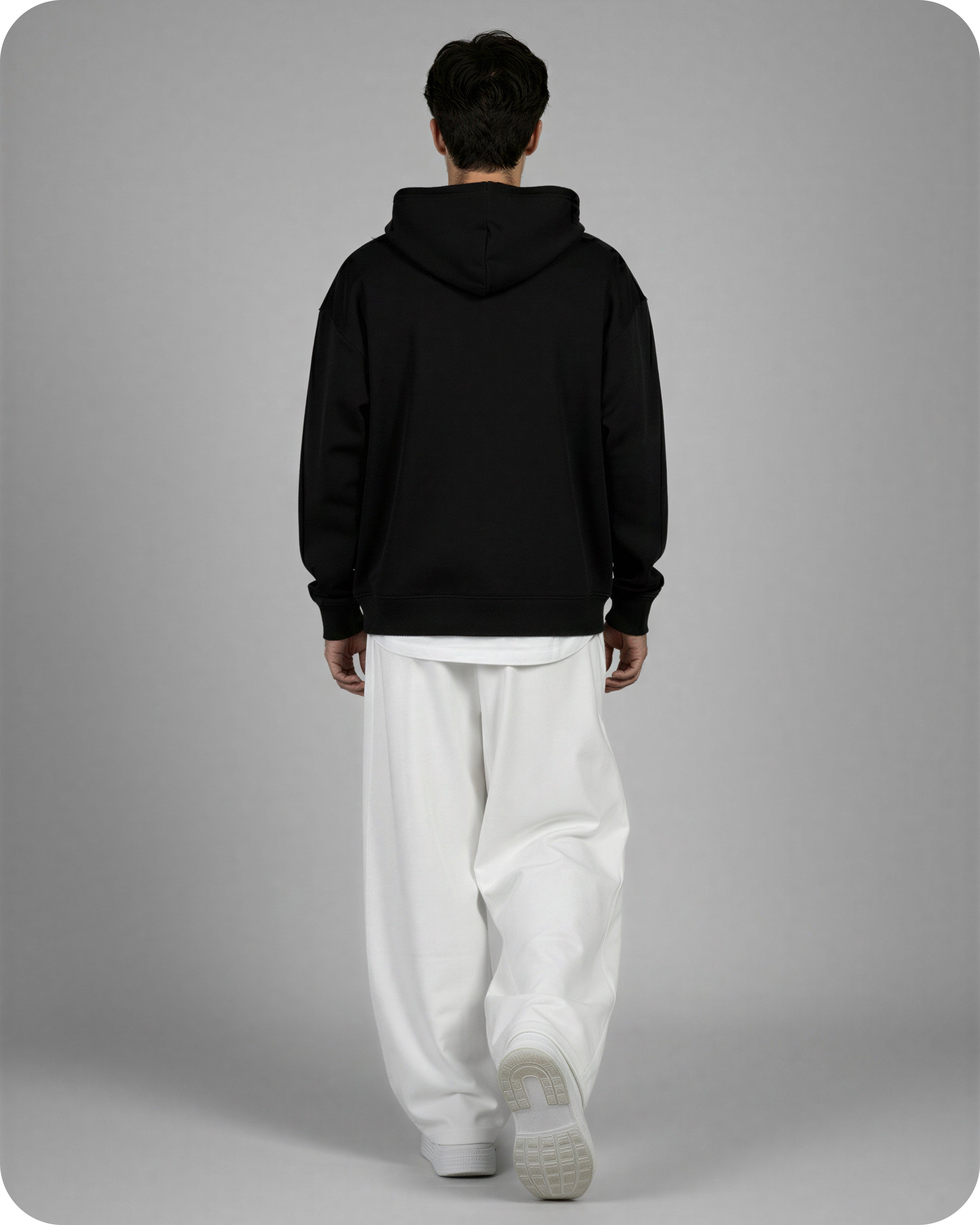 Person wearing a black hoodie and white pants on a gray background