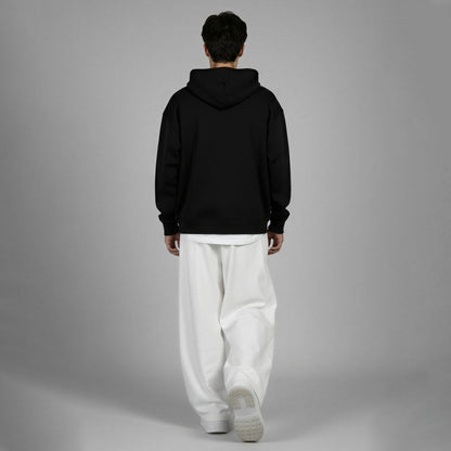Person wearing a black hoodie and white pants on a gray background