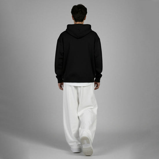 Person wearing a black hoodie and white pants on a gray background