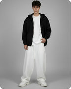 Person wearing a black hoodie, white t-shirt, and white pants on a gray background