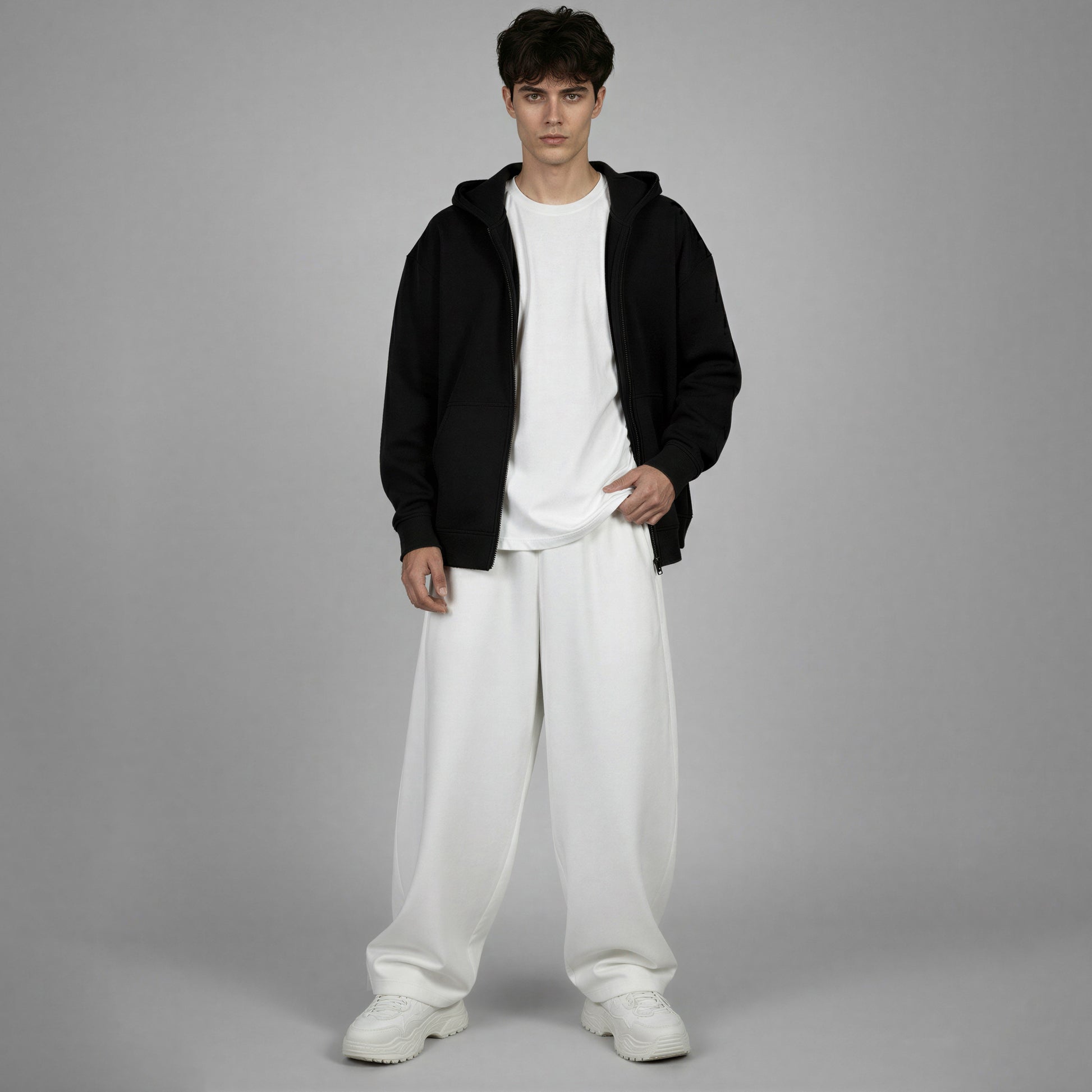 Person wearing a black hoodie, white t-shirt, and white pants on a gray background