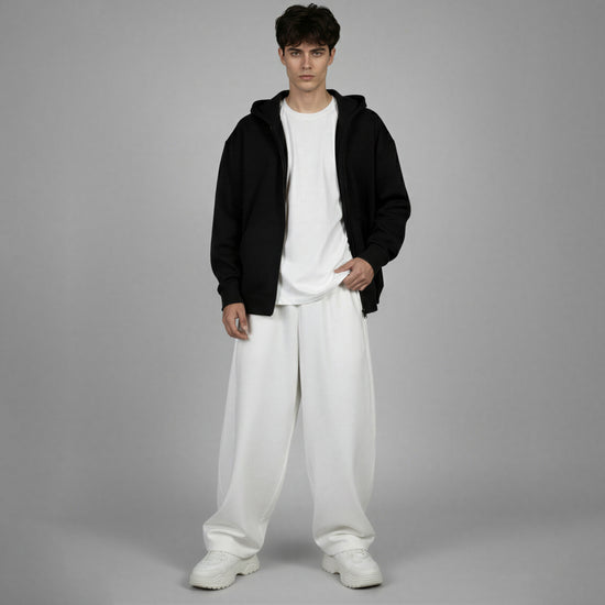 Person wearing a black hoodie, white t-shirt, and white pants on a gray background