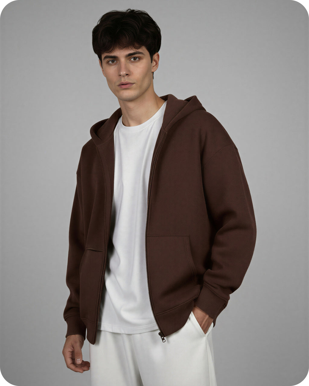 Man wearing a brown hoodie over a white shirt and pants on a gray background