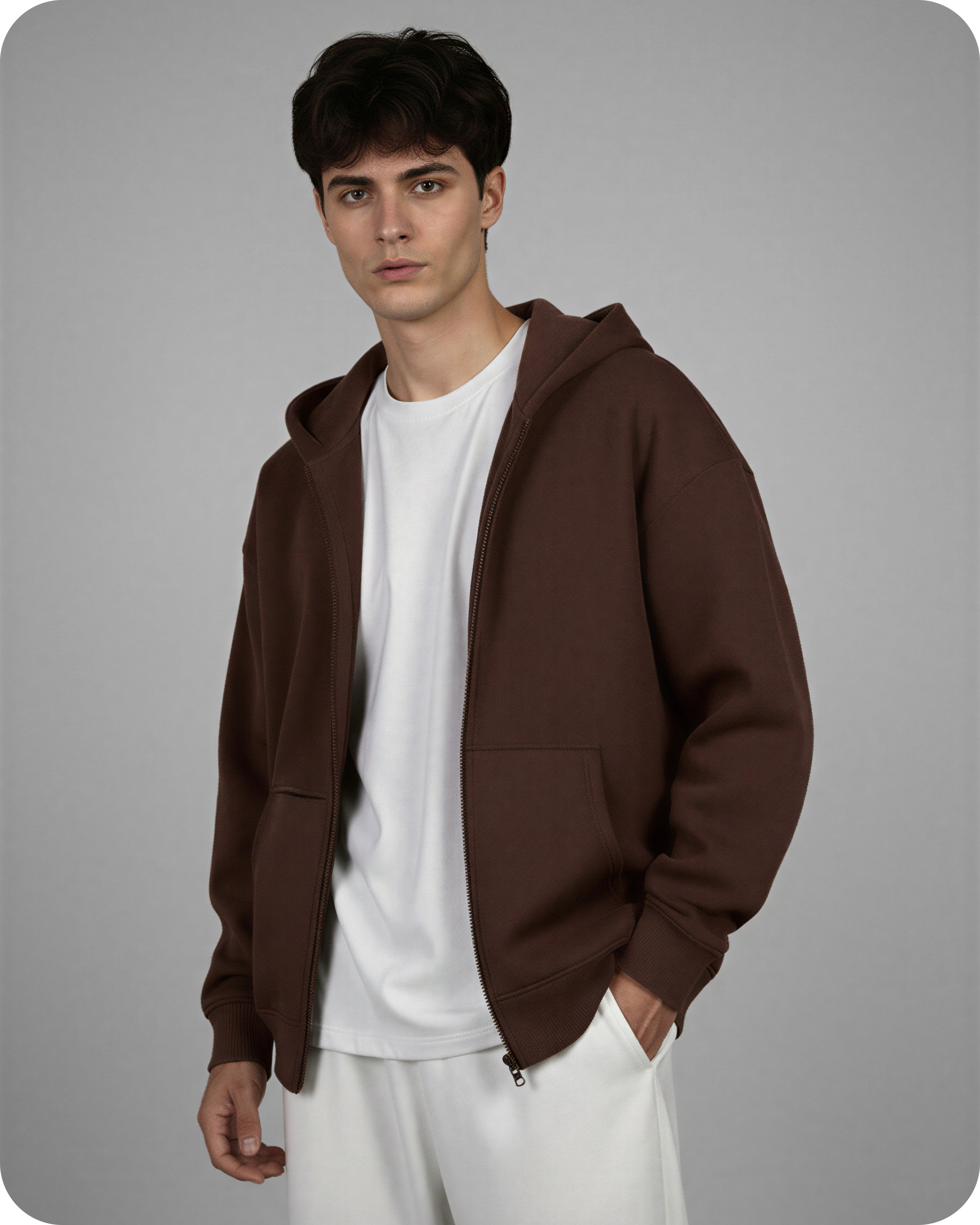 Man wearing a brown hoodie over a white shirt and pants on a gray background