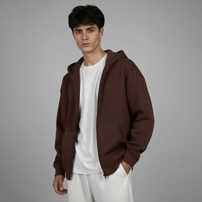 Man wearing a brown hoodie over a white shirt and pants on a gray background