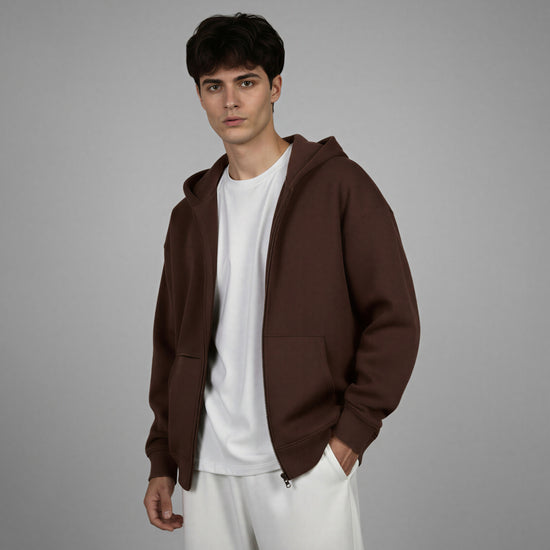Man wearing a brown hoodie over a white shirt and pants on a gray background