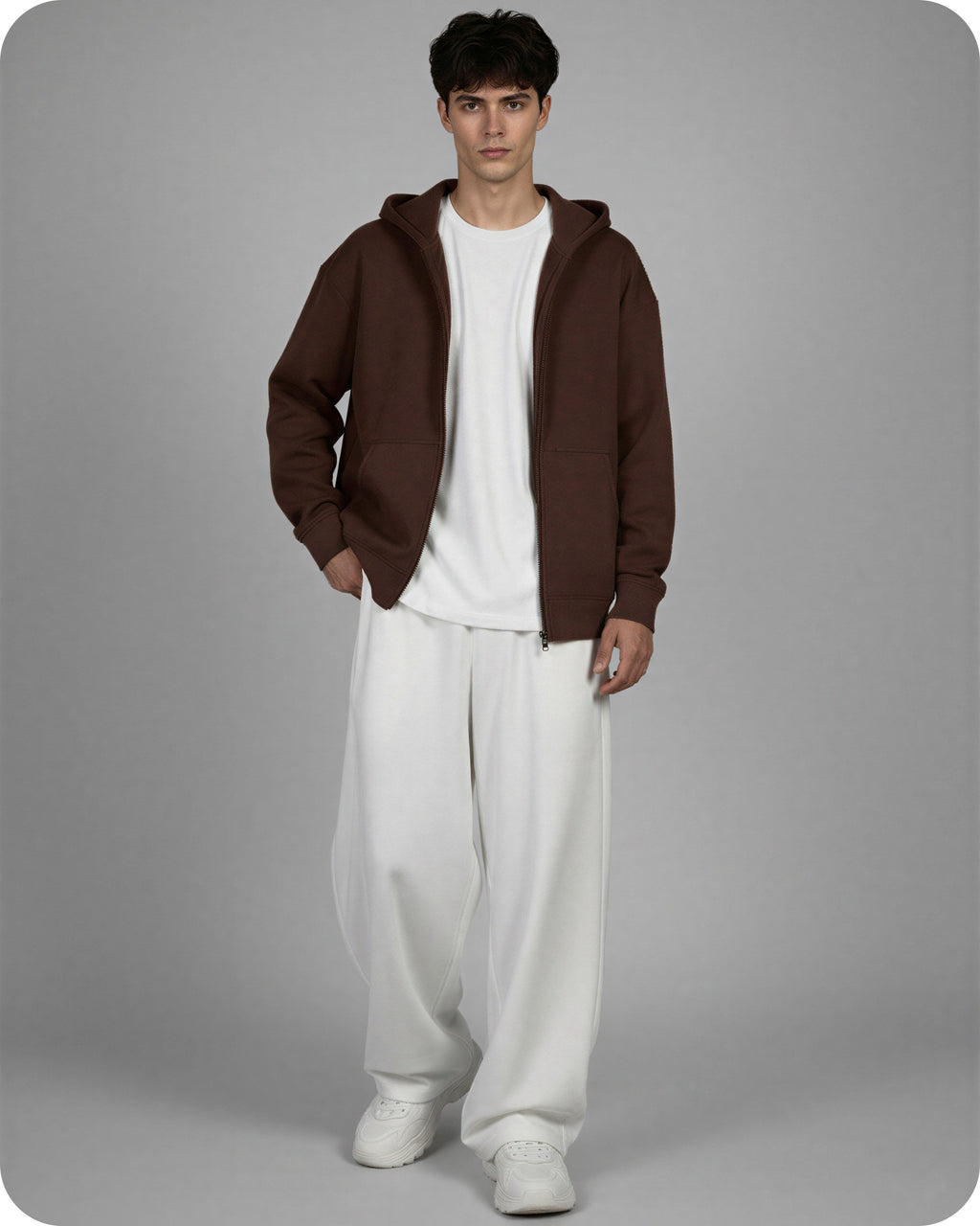 Man wearing a brown hoodie and white pants on a gray background