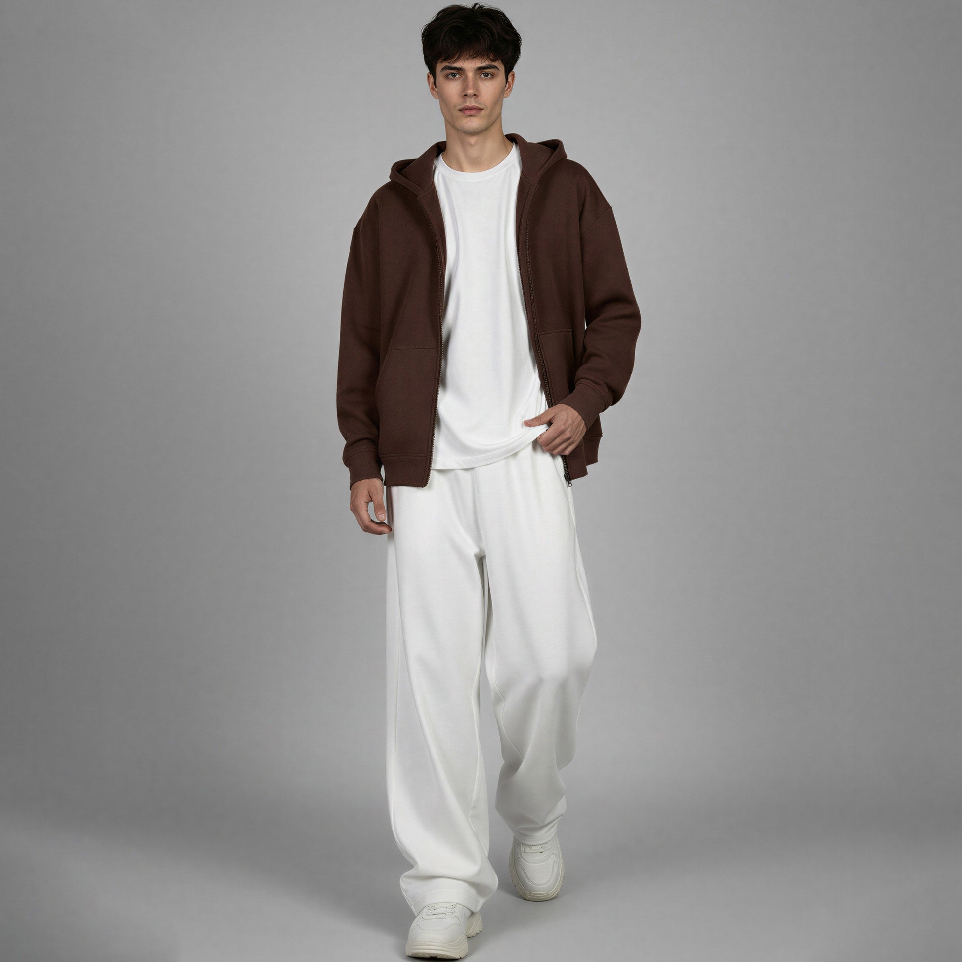 Man wearing a brown hoodie and white pants on a gray background