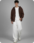 Man wearing a brown hoodie, white shirt, and white pants on a gray background