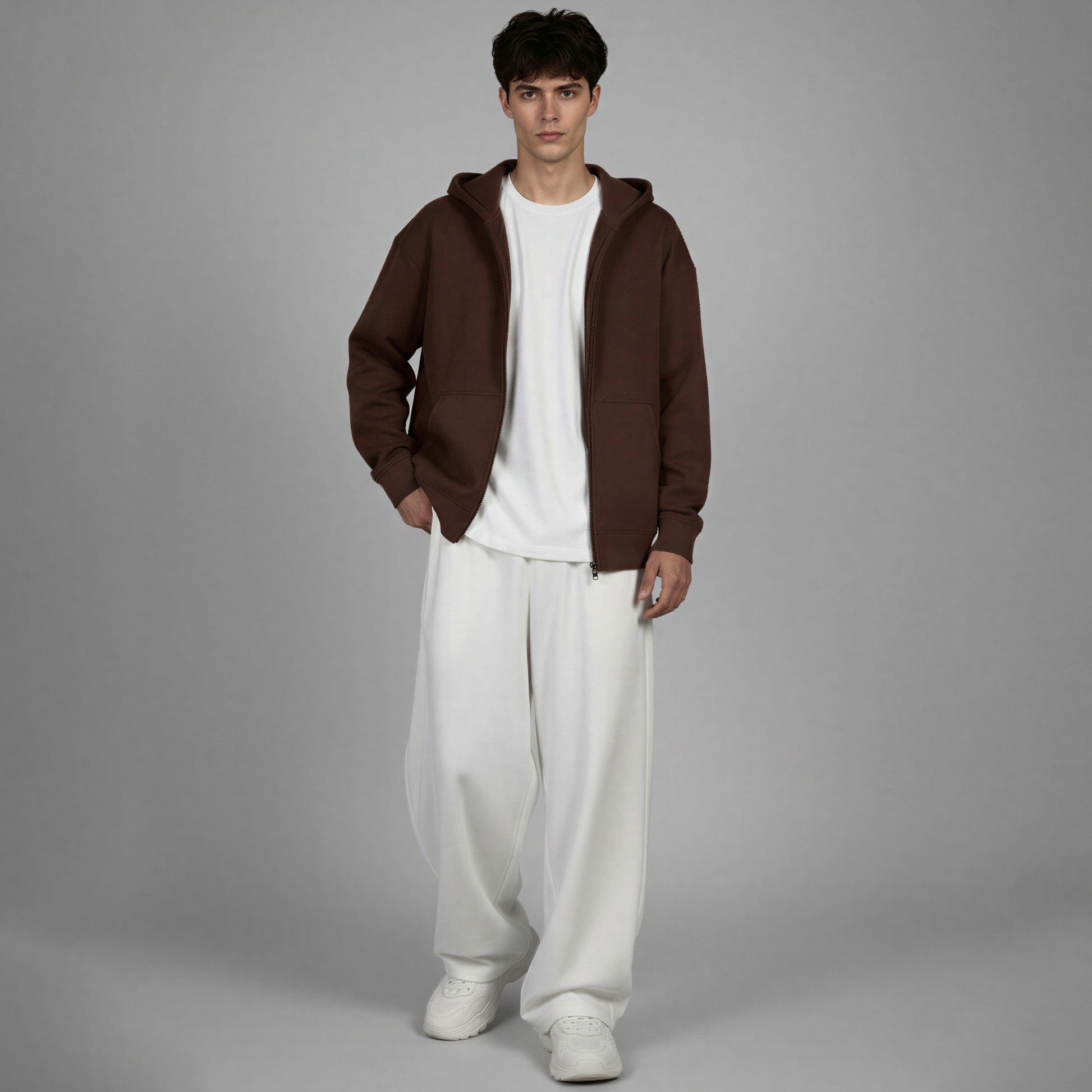 Man wearing a brown hoodie, white shirt, and white pants on a gray background
