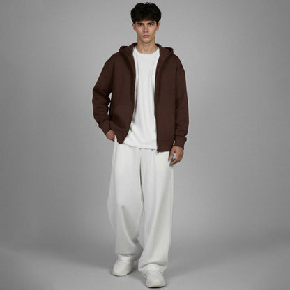 Man wearing a brown hoodie, white shirt, and white pants on a gray background